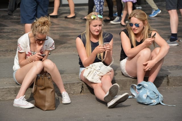 drie jonge meiden zitten op een stoep en kijken op hun telefoon